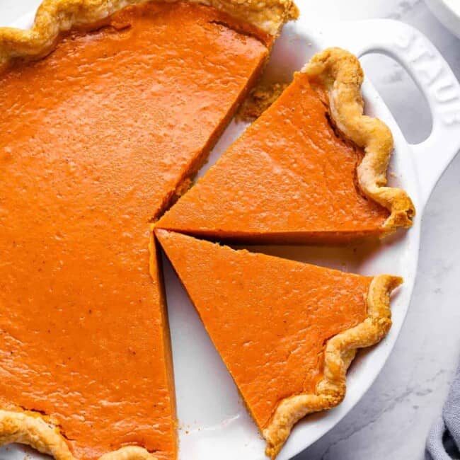 overhead view of a partially sliced sweet potato pie in a white pie pan with handles.