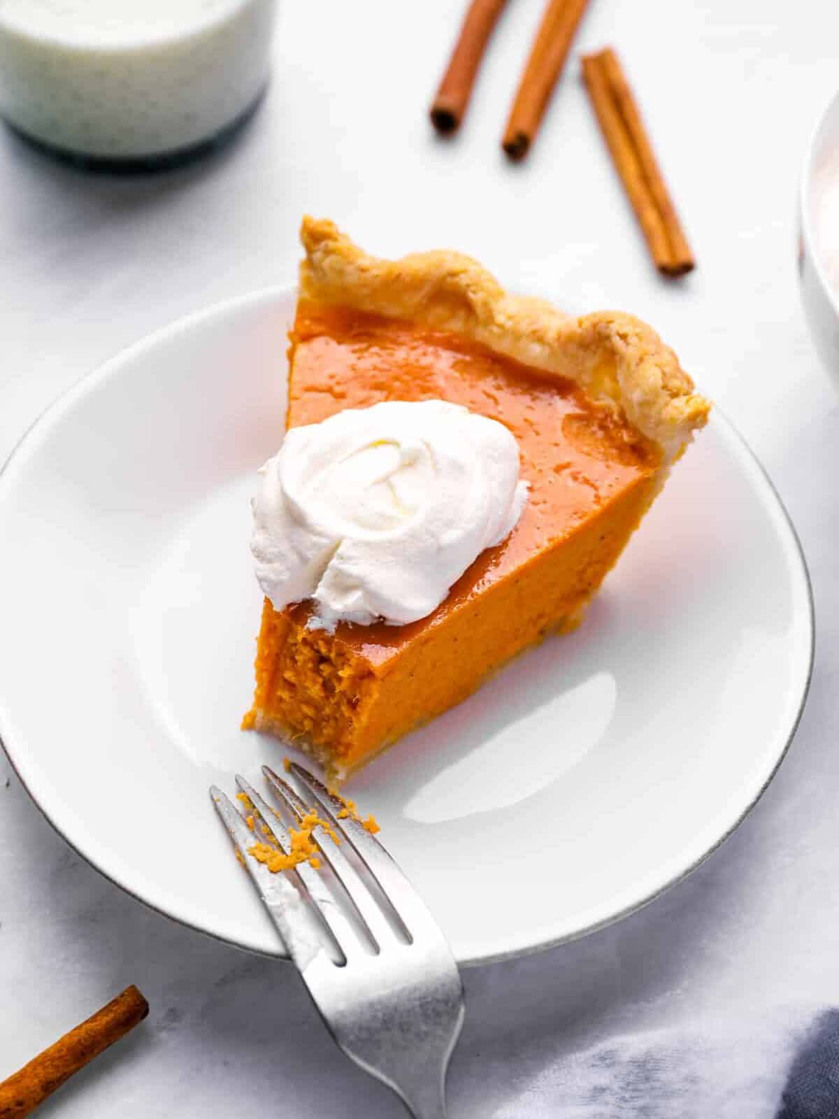 a partially eaten slice of pie on a white plate with a fork and a dollop of whipped cream.