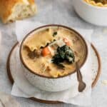 white lasagna soup in a white and brown bowl on a plate with a spoon.