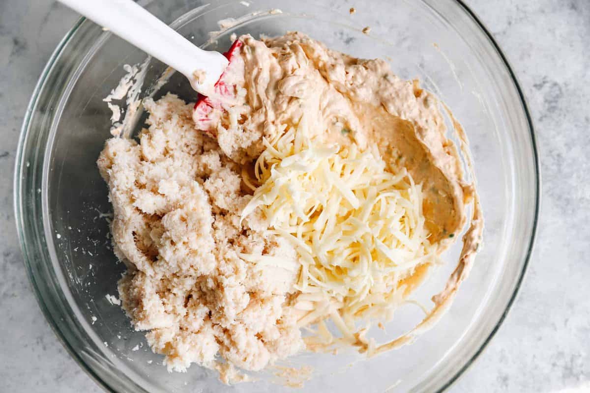 crab meat and cheese in a glass bowl with a rubber spatula.