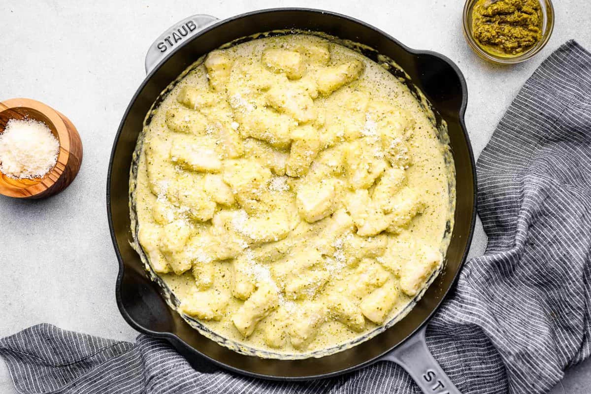 overhead view of gnocchi in pesto cream sauce in a cast iron skillet.