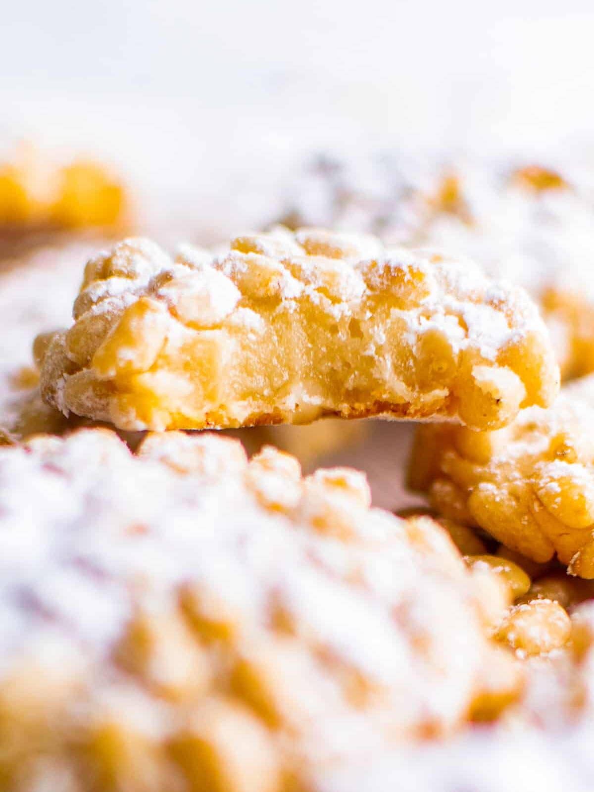 close up view of a partially eaten cookie with pine nuts and powdered sugar.