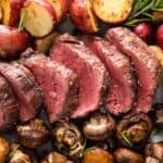 sheet pan with slices of beef tenderloin and roasted red potatoes and mushrooms