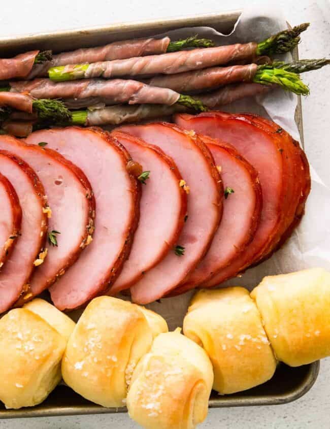 ham, prosciutto wrapped asparagus, and rolls on a sheet pan after baking