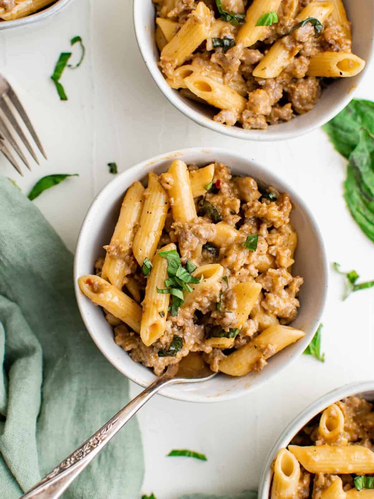 overhead view of sausage pasta in white bowls with forks.