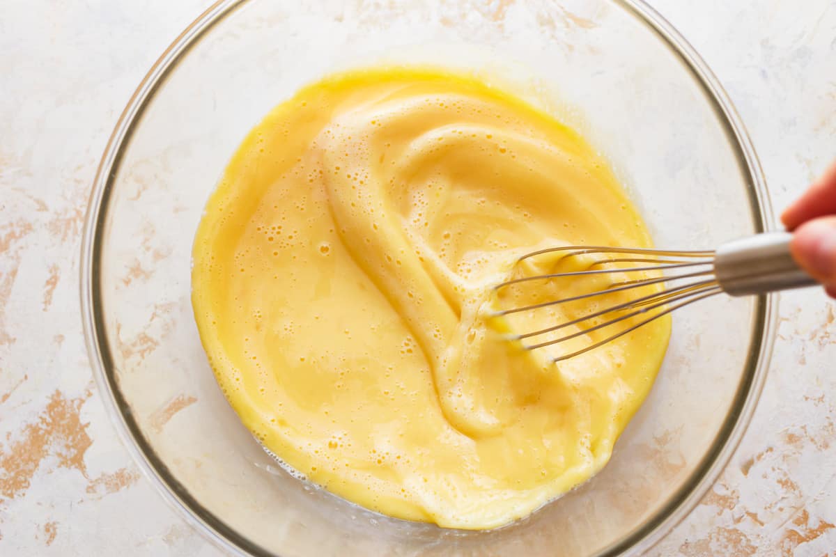 A person whisking egg mixture in a glass bowl.