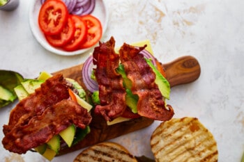 Avocado burgers on a wooden cutting board with crispy bacon.