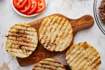 Four avocado burgers on a wooden cutting board.