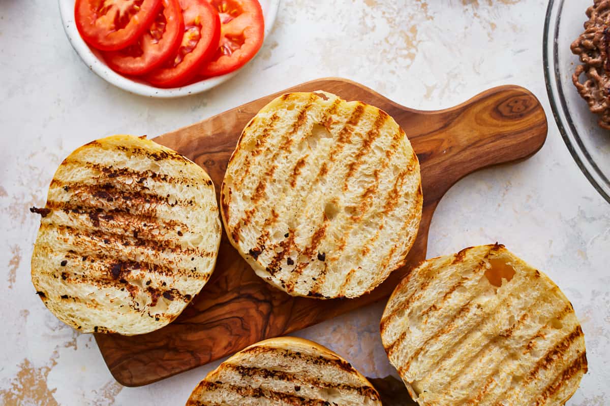 Grilled burger buns on a cutting board.