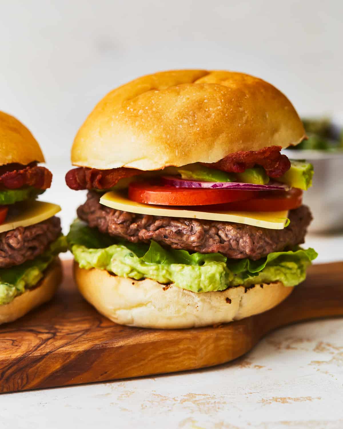 Two avocado burgers on a wooden cutting board.