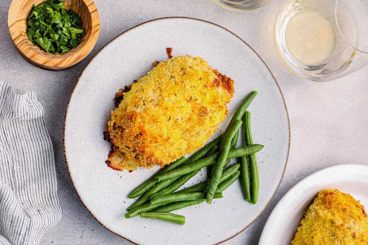 chicken cordon bleu baked on a white plate with green beans.