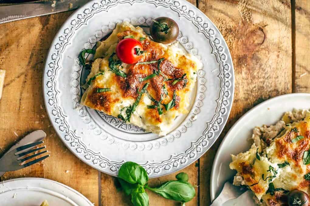 plates of white caprese lasagna topped with tomatoes.