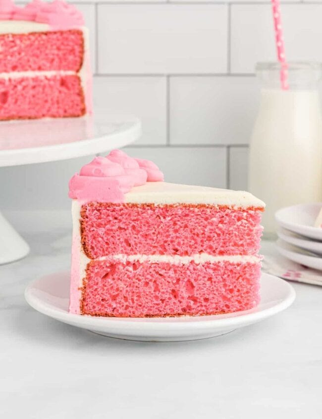 side view of a slice of pink velvet cake on a white plate.