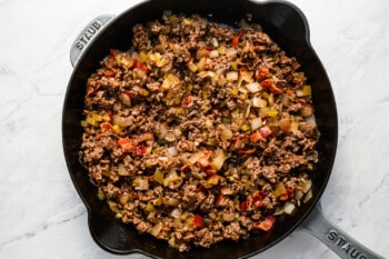 Cheeseburger bombs cooked in a skillet with ground beef and vegetables.