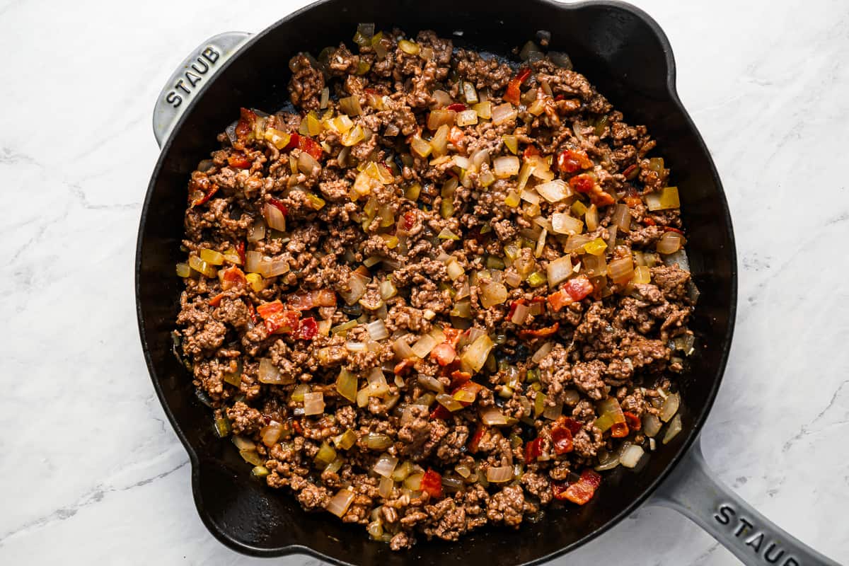 Cheeseburger filling, with onions, ketchup, and pickles, cooking in a skillet.