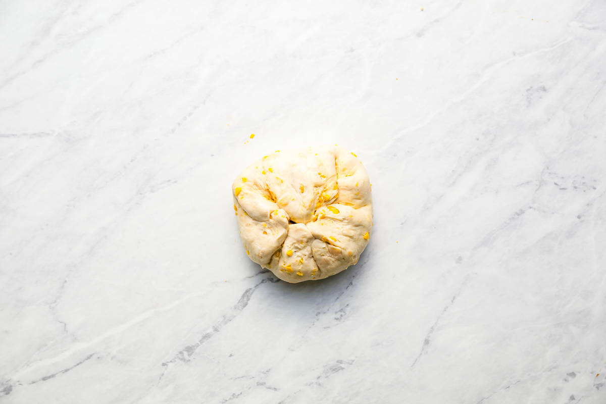 A ball of uncooked biscuit dough on a marble surface.