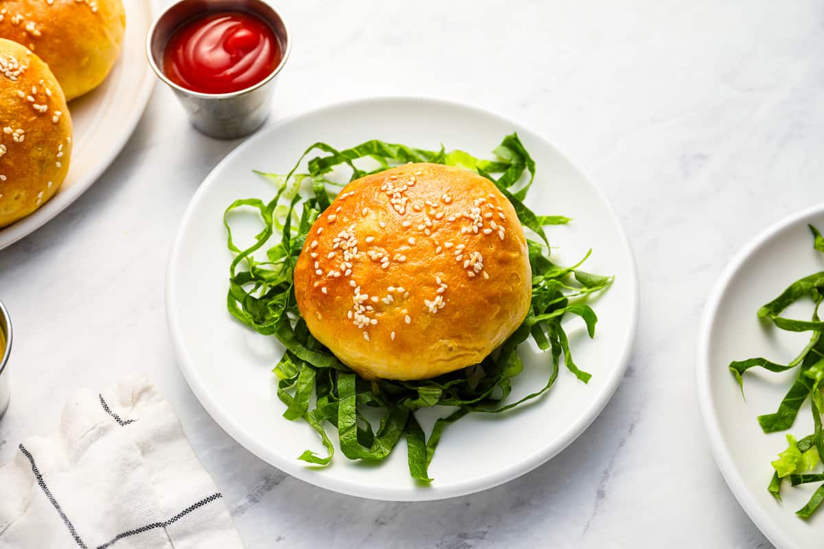 A biscuit dough cheeseburger bomb on a white plate, next to a small dish of ketchup.