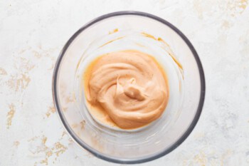 A bowl of orange sauce in a glass on a white background, perfect for dipping bagel breakfast sandwiches.