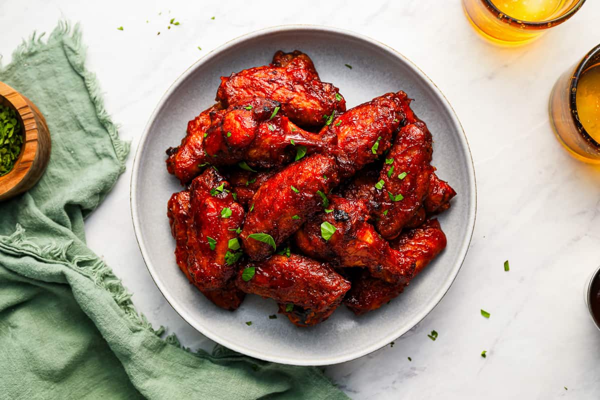 Barbecue chicken wings on a plate next to a glass of beer.