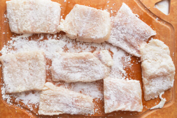 A cutting board with pieces of beer-battered fish on it.