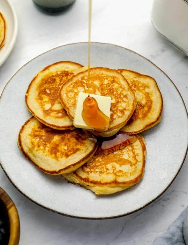 three-quarters view of a plate full of homemade pancakes with butter and syrup.