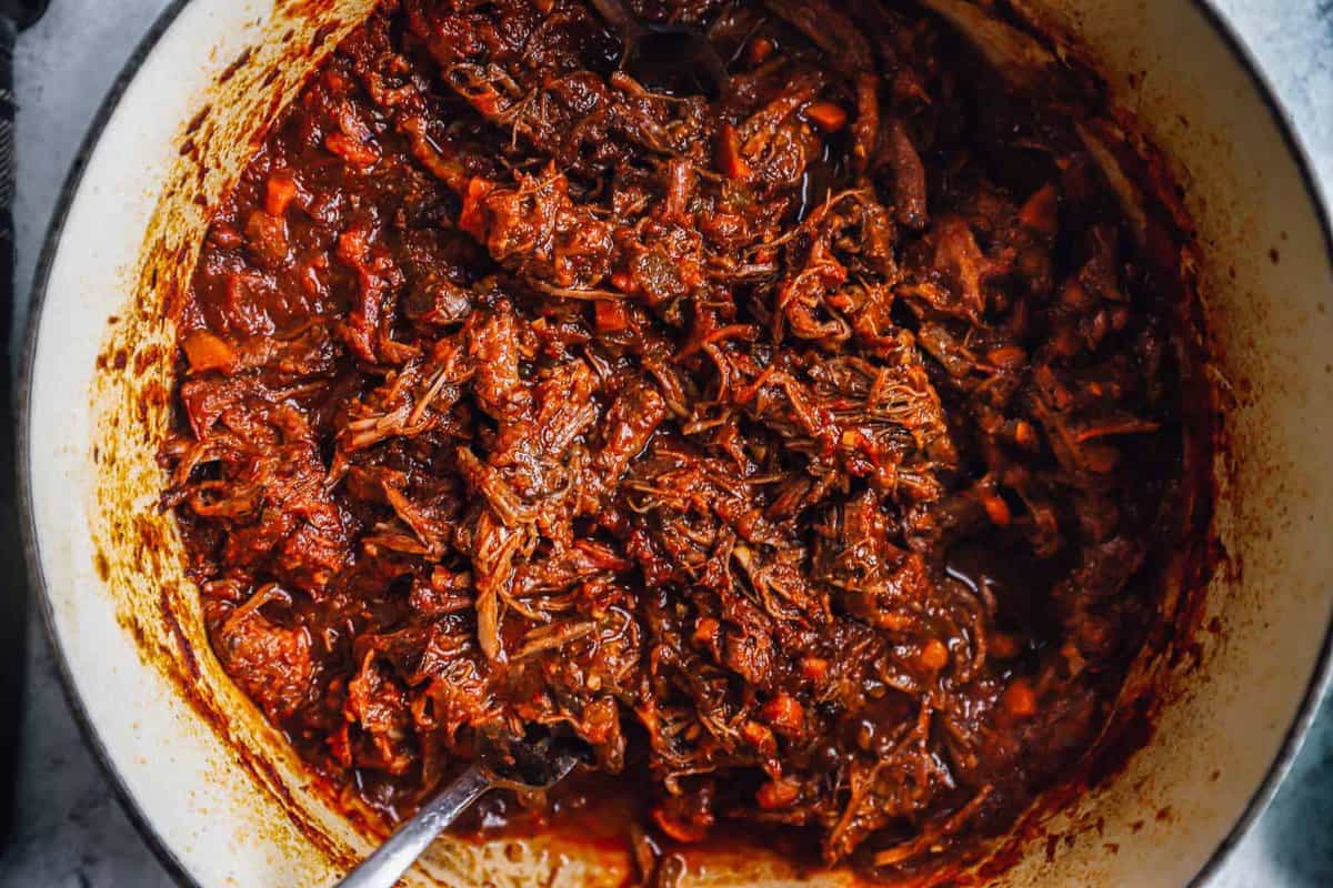 beef ragu in a dutch oven with a spoon.