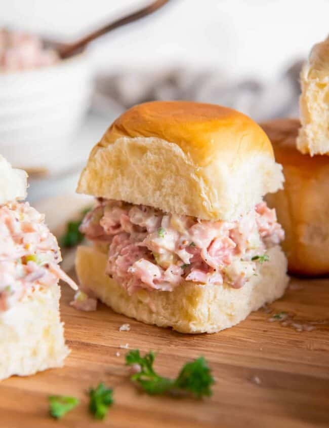 ham salad on slider rolls on a wooden cutting board.