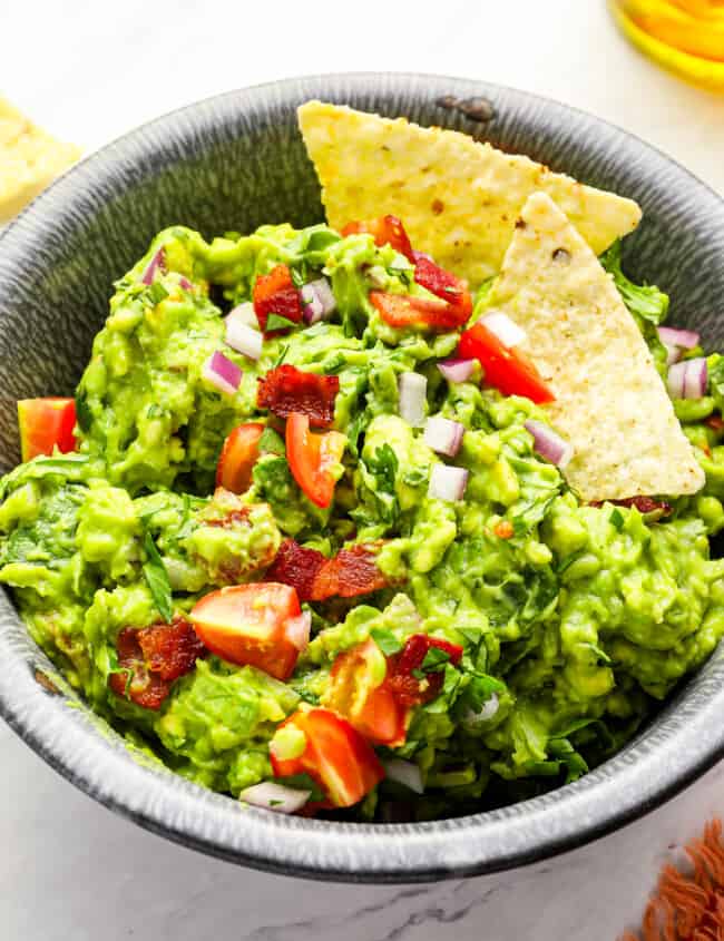 close up of blt guacamole in a bowl with tortilla chips.