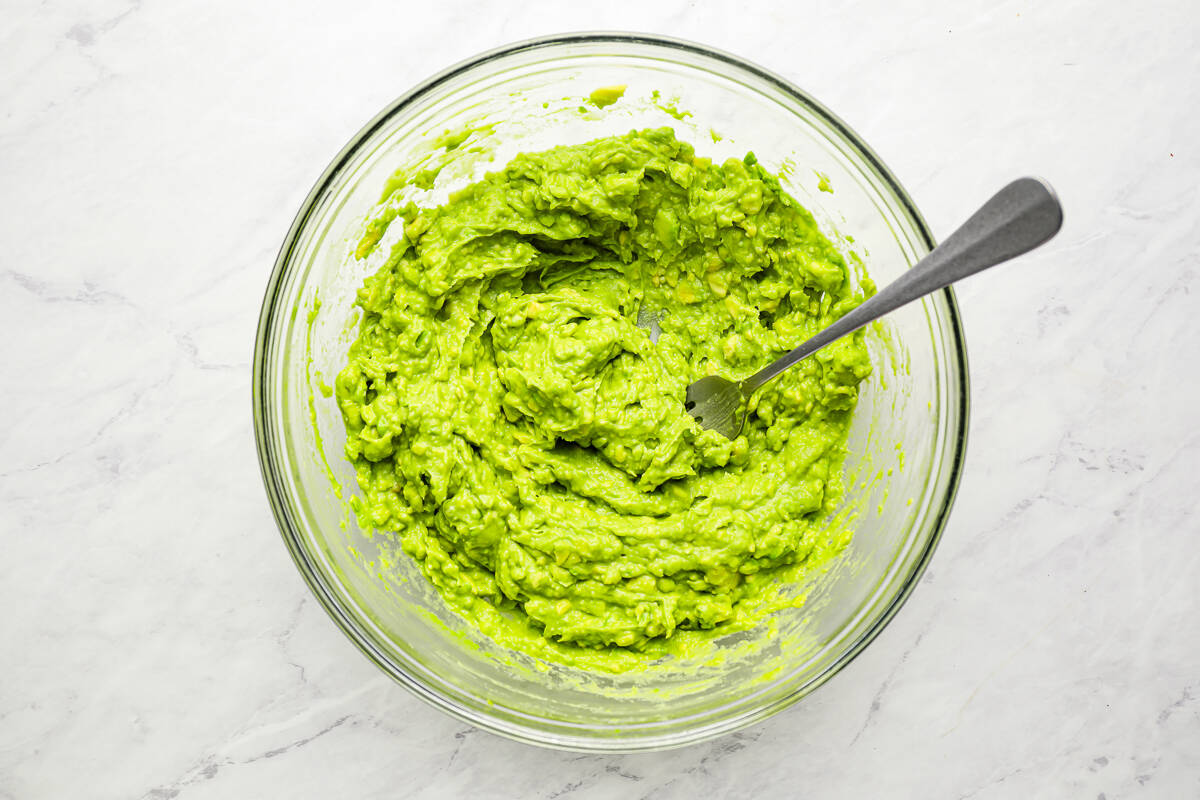 mashed avocado in a glass bowl with a fork.