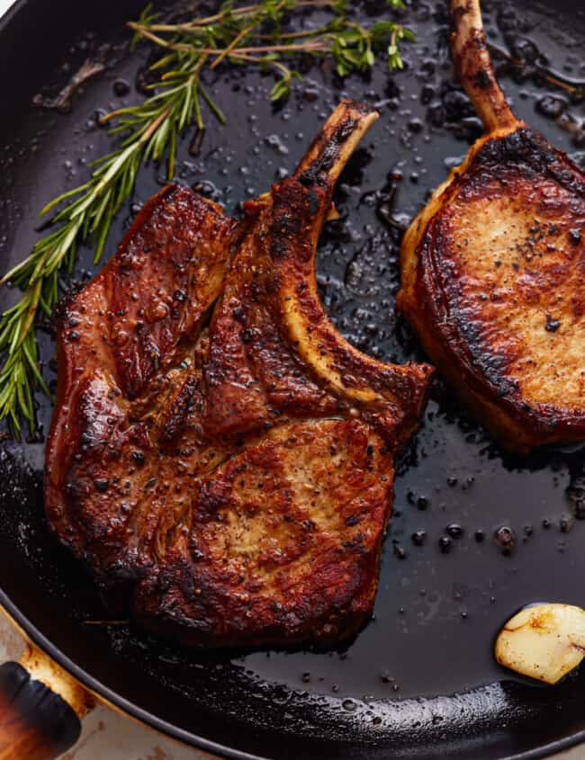 overhead view of seared bone in pork chops in a cast iron pan with herbs and garlic.