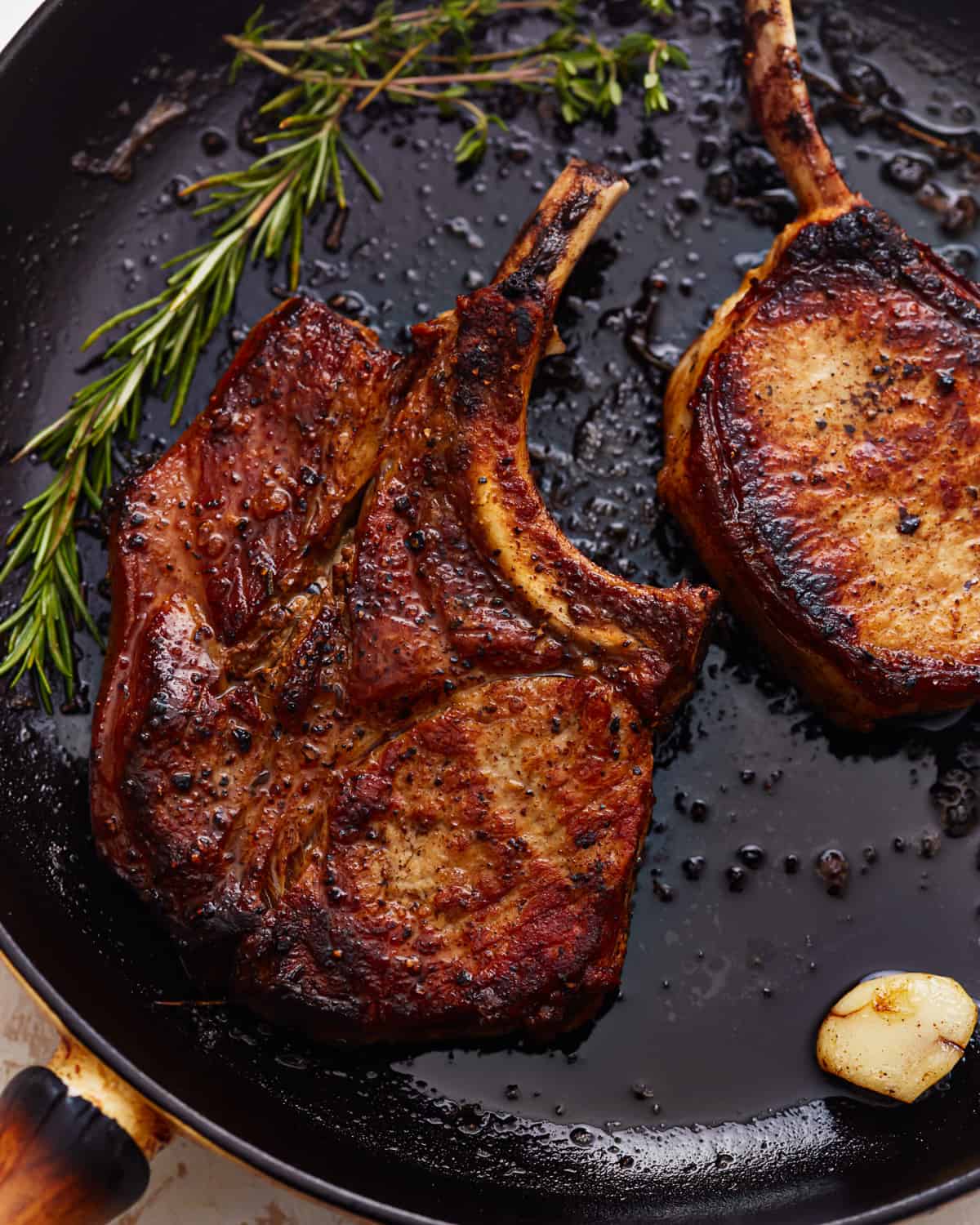 overhead view of seared bone in pork chops in a cast iron pan with herbs and garlic.