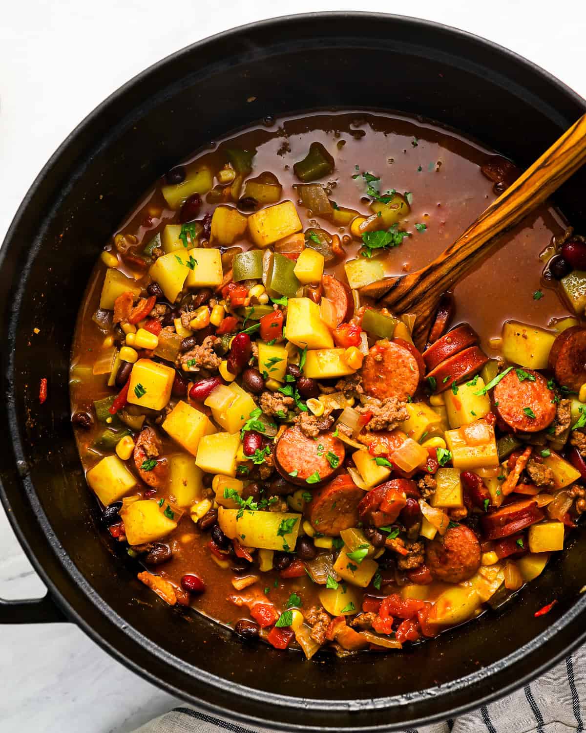 overhead view of cowboy stew in a dutch oven with a wooden spoon.