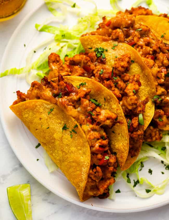 close-up view of 4 crispy chicken tacos on a white plate.