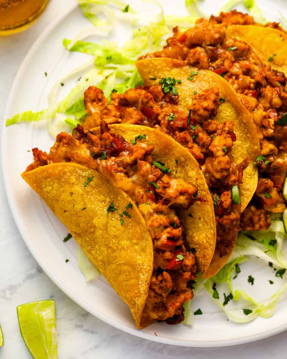 close-up view of 4 crispy chicken tacos on a white plate.