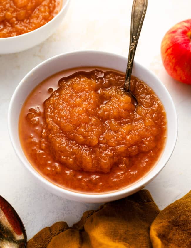 a serving of applesauce in a white bowl with a spoon.