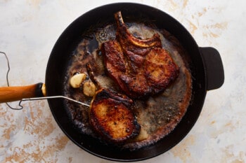 overhead view of a temperature probe inserted in a pork chop in a cast iron skillet.