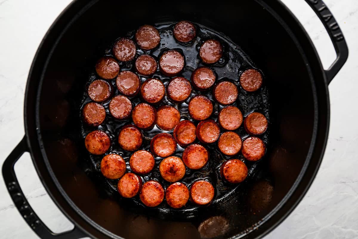 slices of kielbasa cooking in a dutch oven.