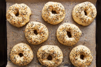 8 everything bagel seasoned unbaked bagels on a baking sheet.