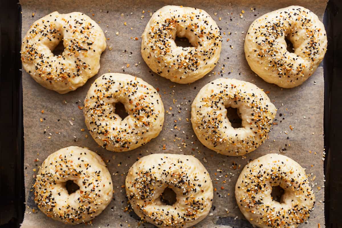 8 everything bagel seasoned unbaked bagels on a baking sheet.