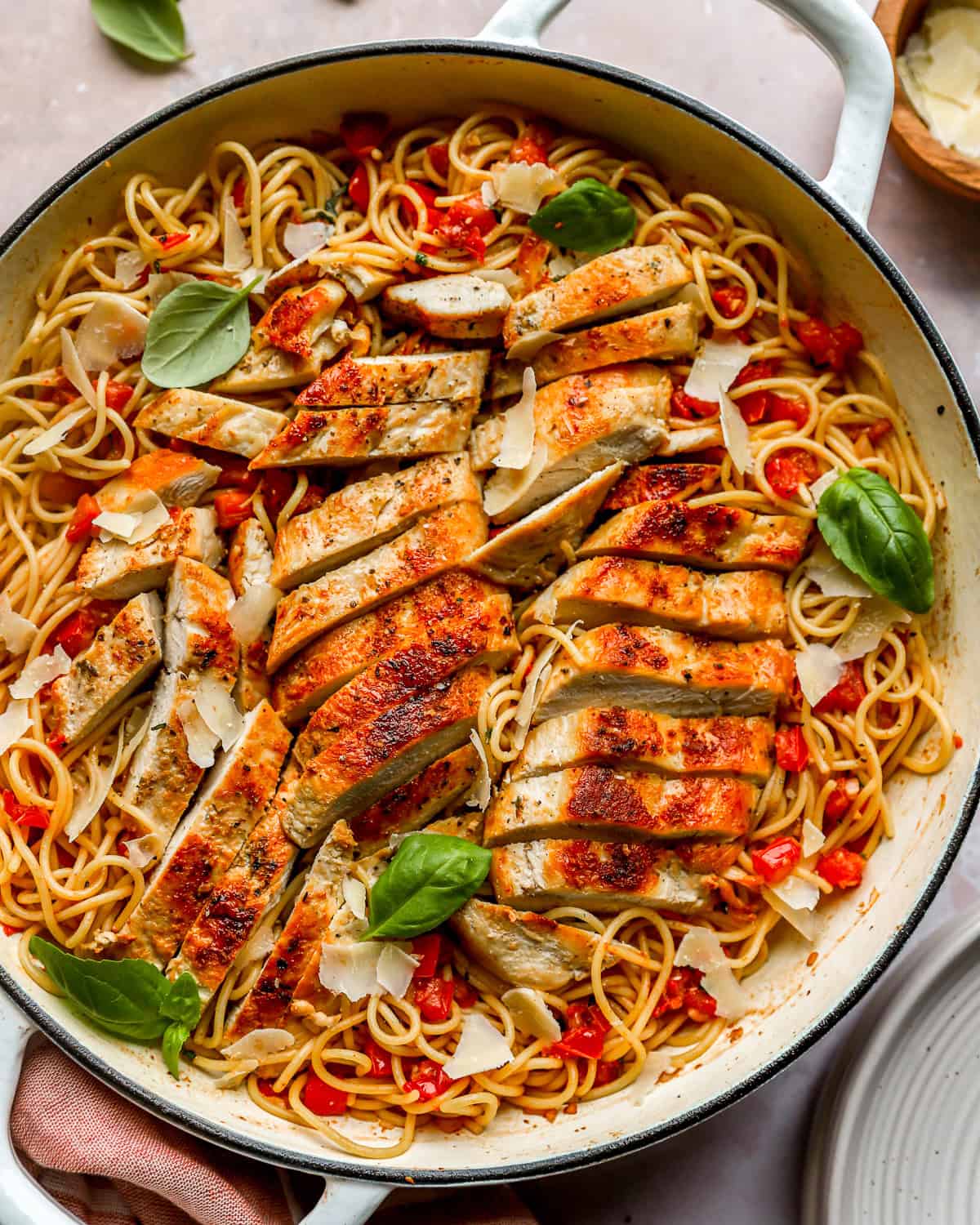 A pot of bruschetta chicken pasta with angel hair pasta, tomatoes, basil, and sliced chicken breasts.