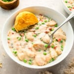 A bowl of creamy Chicken a la King, with a half-eaten biscuit on the side.