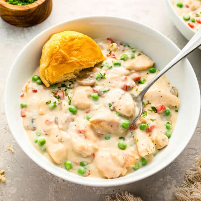 A bowl of creamy Chicken a la King, with a half-eaten biscuit on the side.