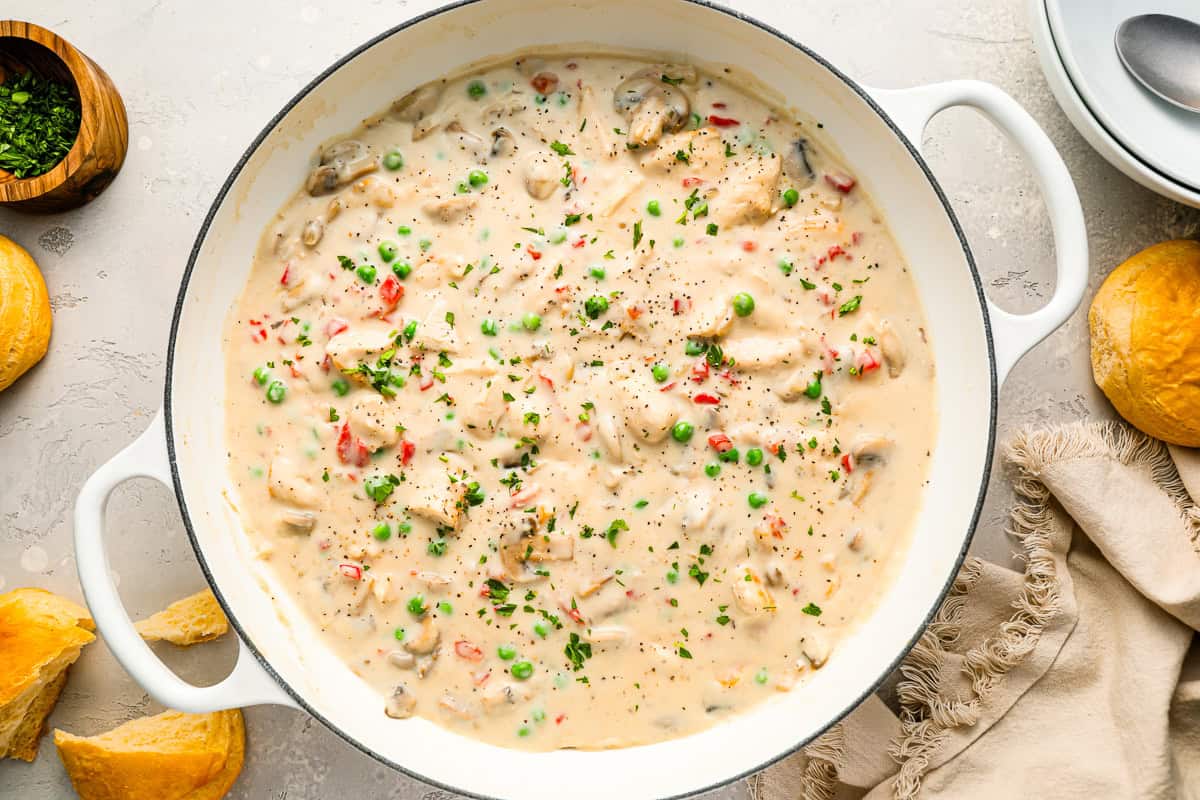 A pot full of creamy stew with chicken, peas, mushrooms, and more.