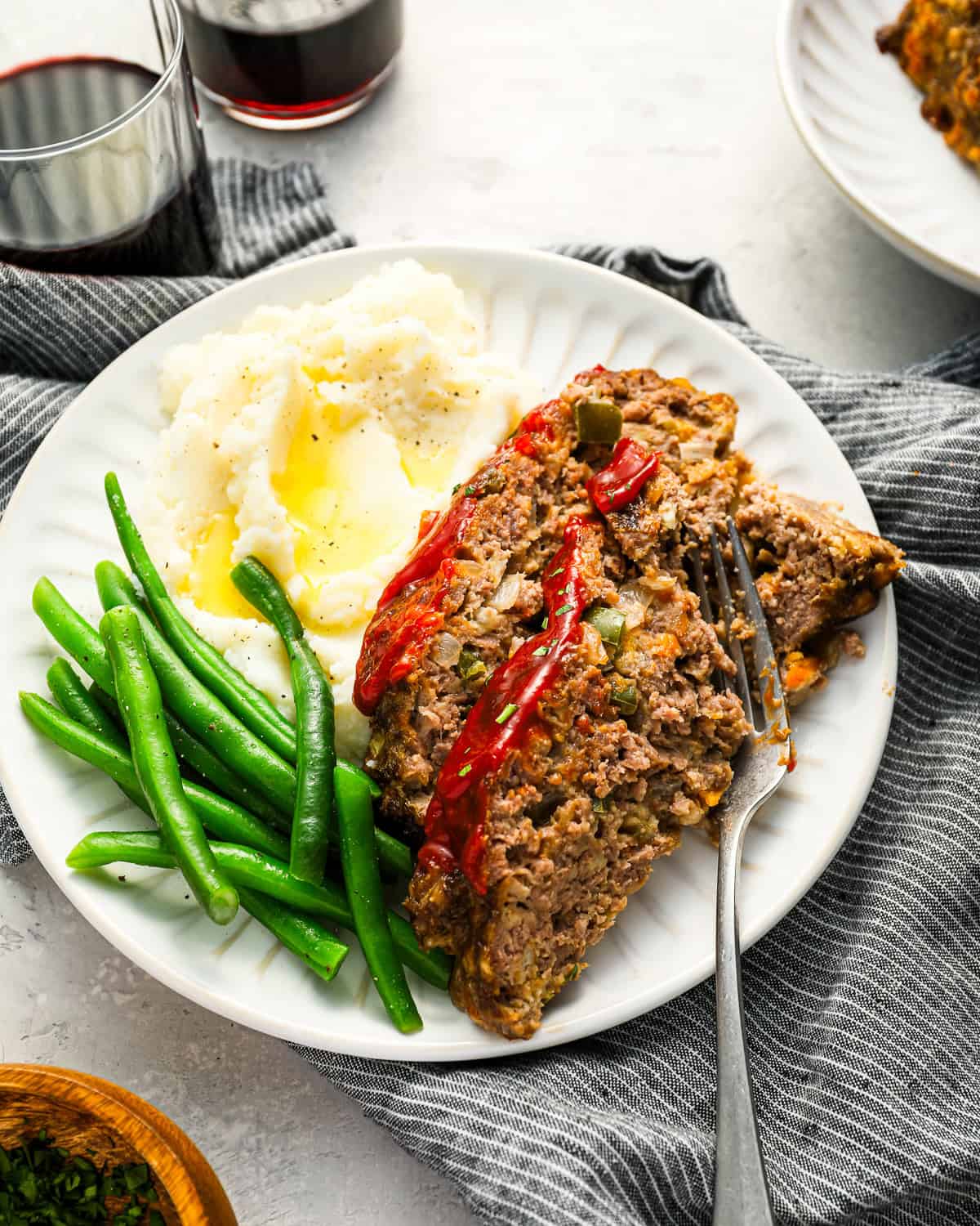 2 slices of cracker barrel meatloaf on a white plate with green beans, mashed potatoes, and a fork.