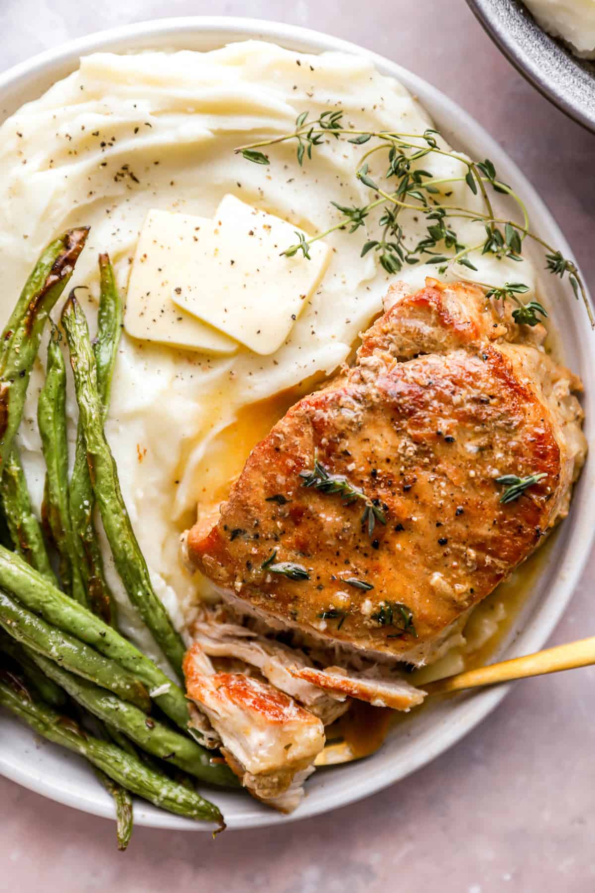 close up view of a crockpot pork chop on a white plate with green beans and mashed potatoes.