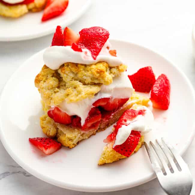 cut strawberry shortcake on a white plate with a fork.