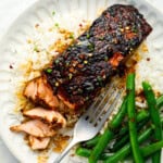 overhead view of a partially eaten serving of firecracker salmon on a white plate with green beans and a fork.