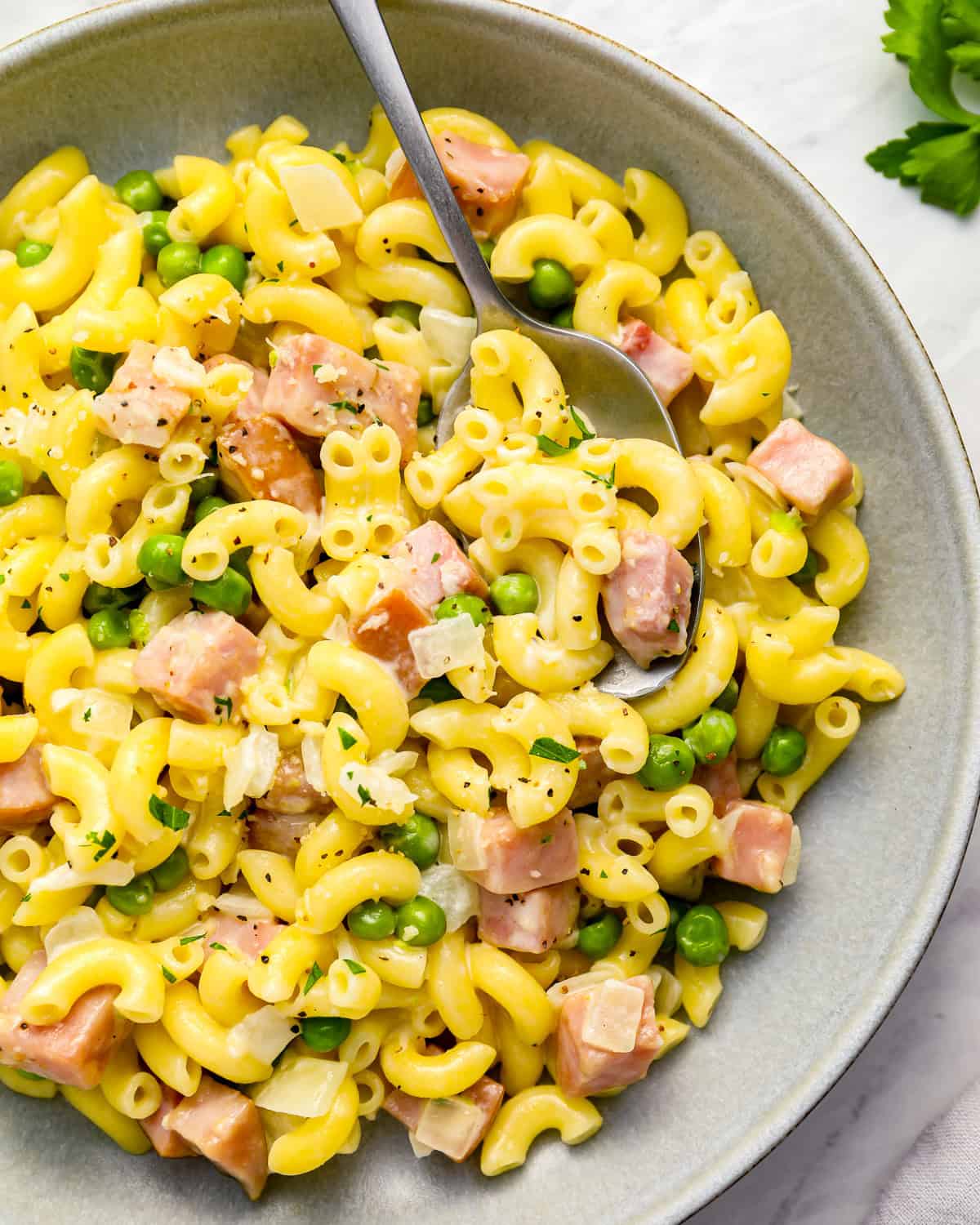 overhead view of a serving of ham and pea pasta in a gray bowl with a fork.