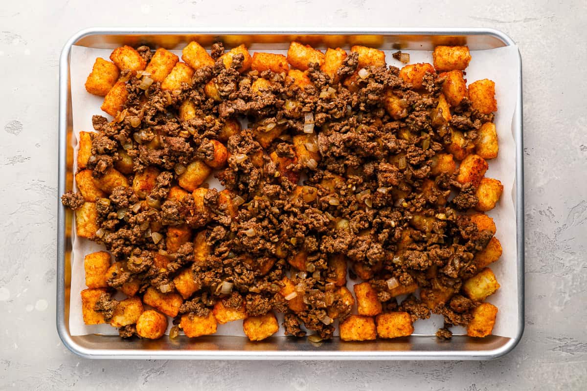 cooked ground beef over tater tots on a baking sheet.