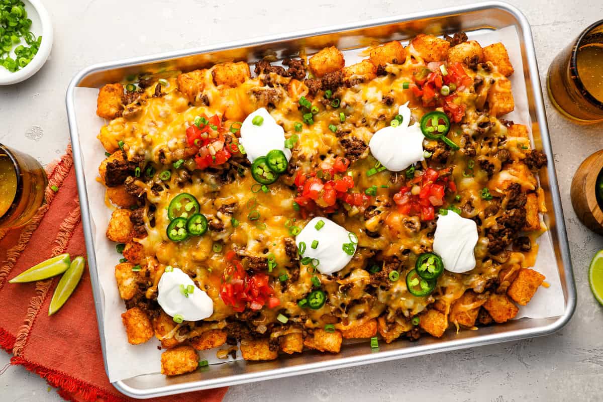 loaded tater tots on a baking sheet with dollops of sour cream.